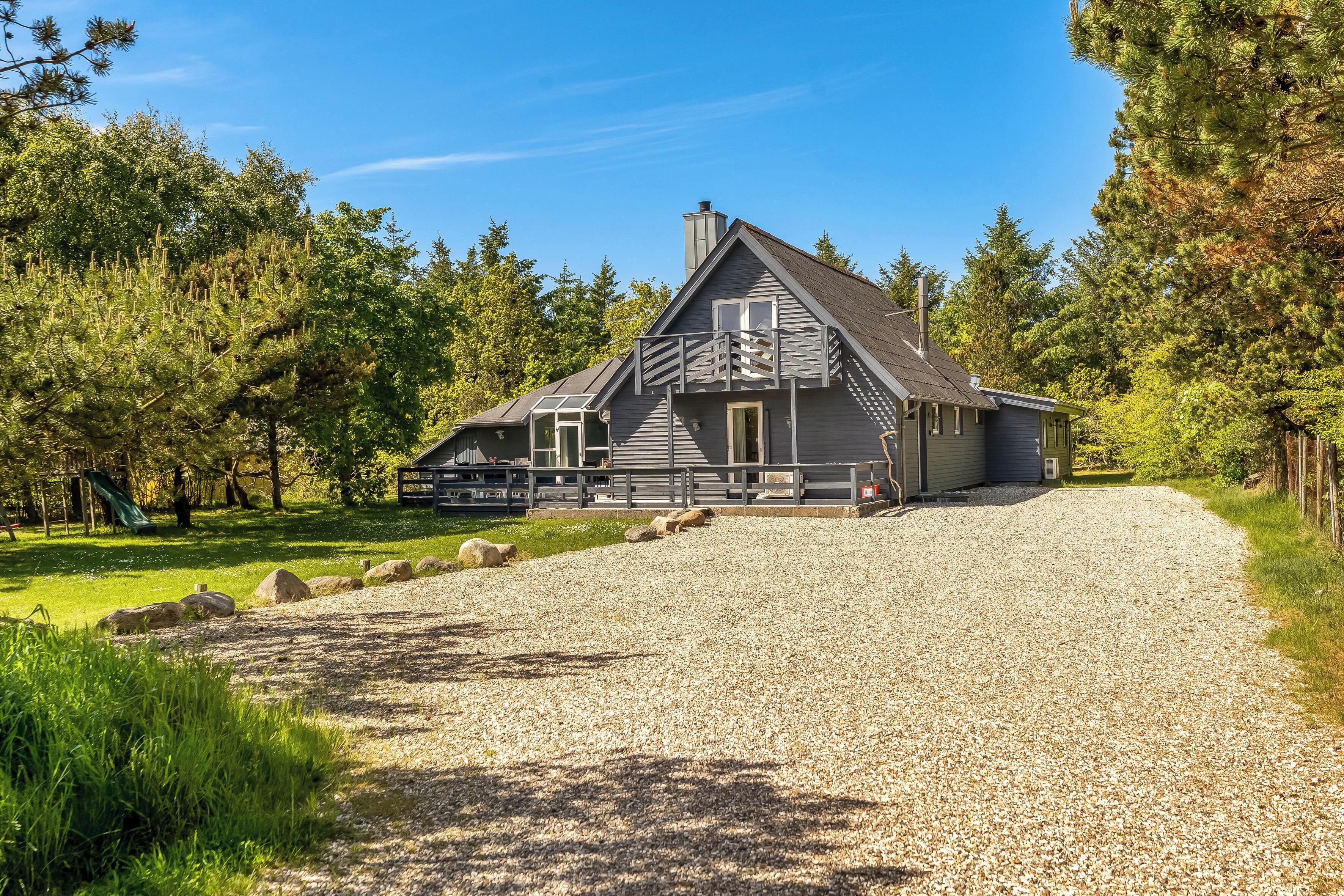 Une maison avec une allée en gravier, une terrasse en bois et une cour clôturée.