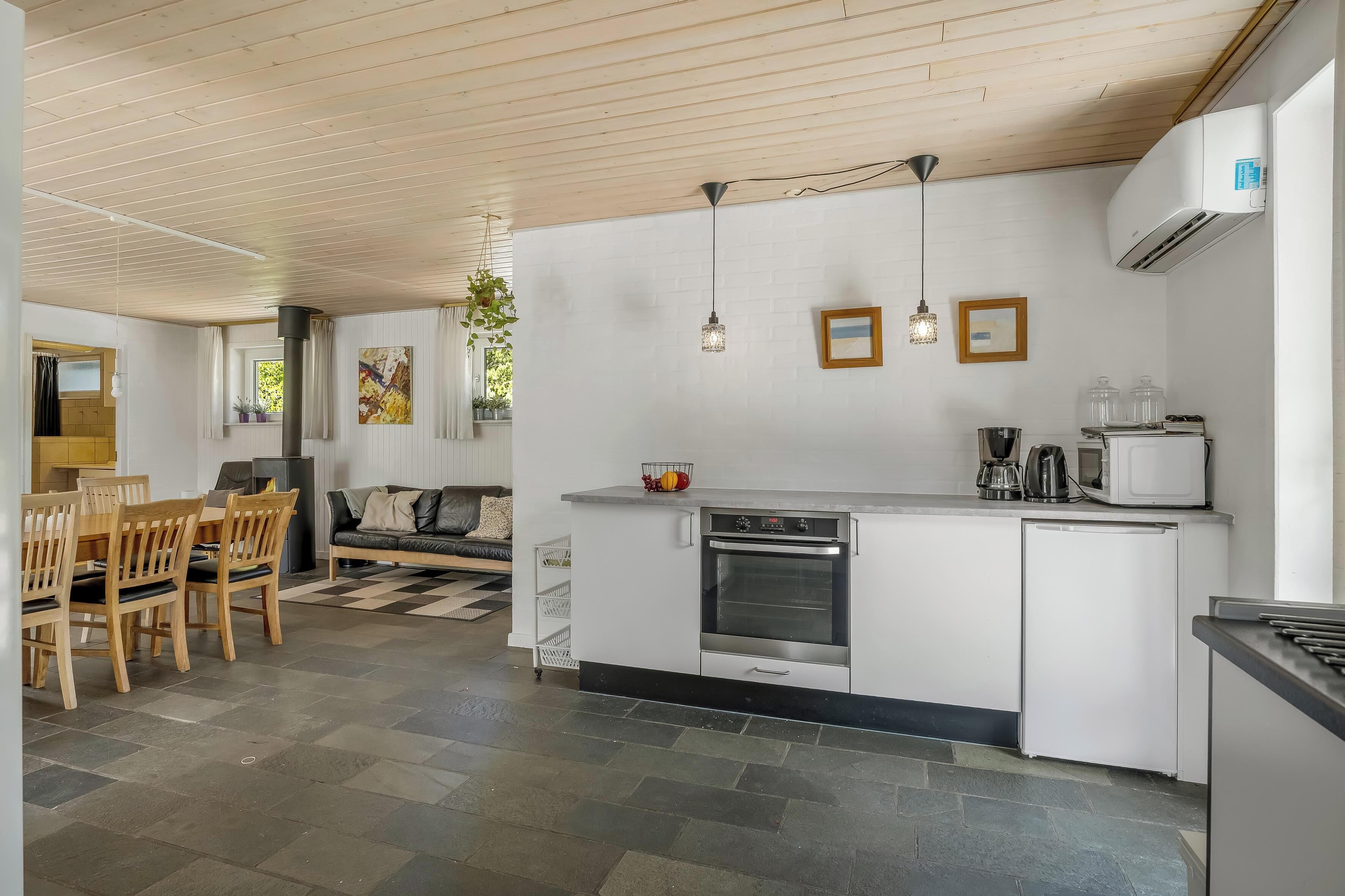 Une cuisine moderne équipée d’un four encastré, d’un four à micro-ondes et d’un réfrigérateur. On y trouve également un coin repas avec une table et des chaises en bois.