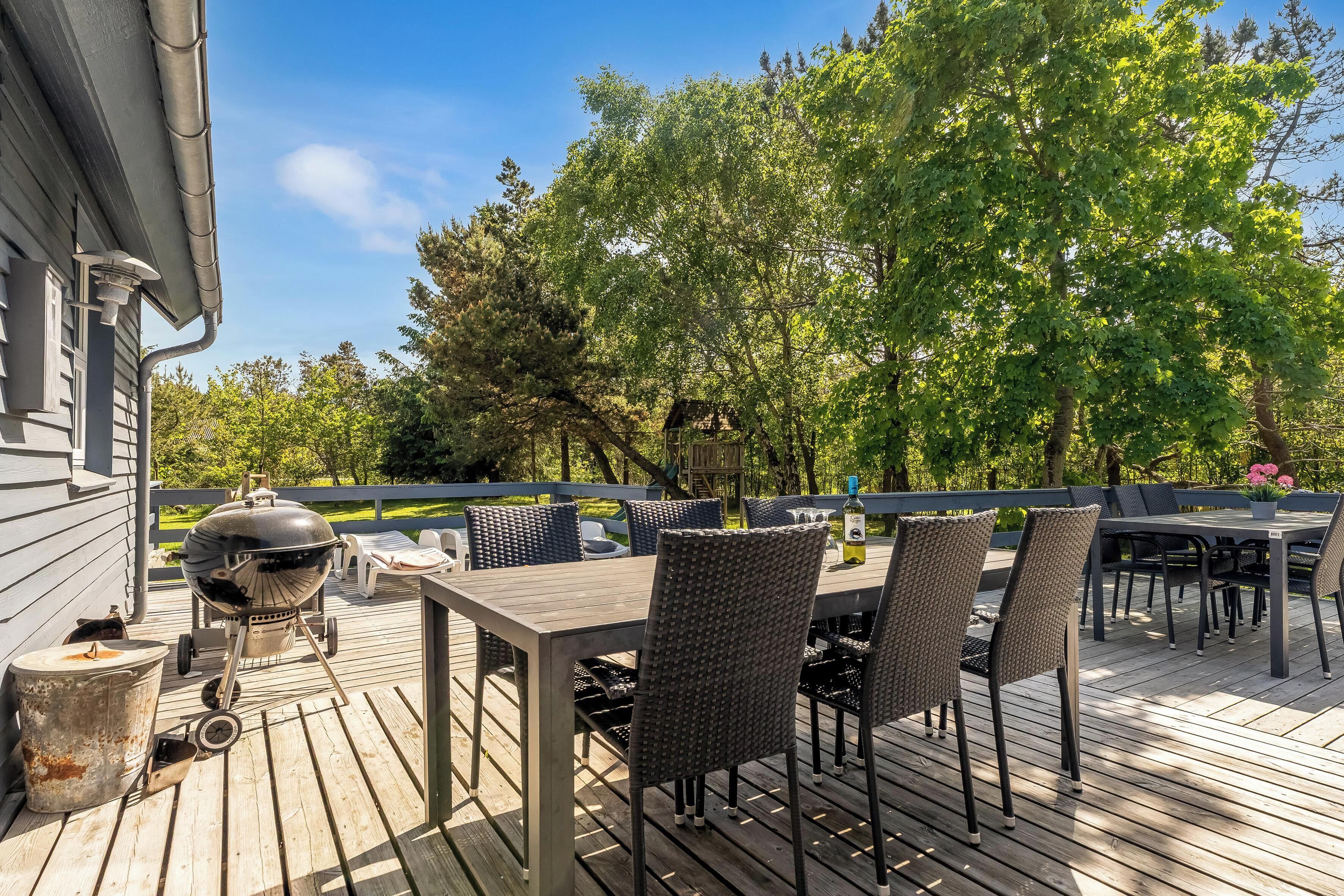 A wooden deck with a grill, dining table, and chairs.