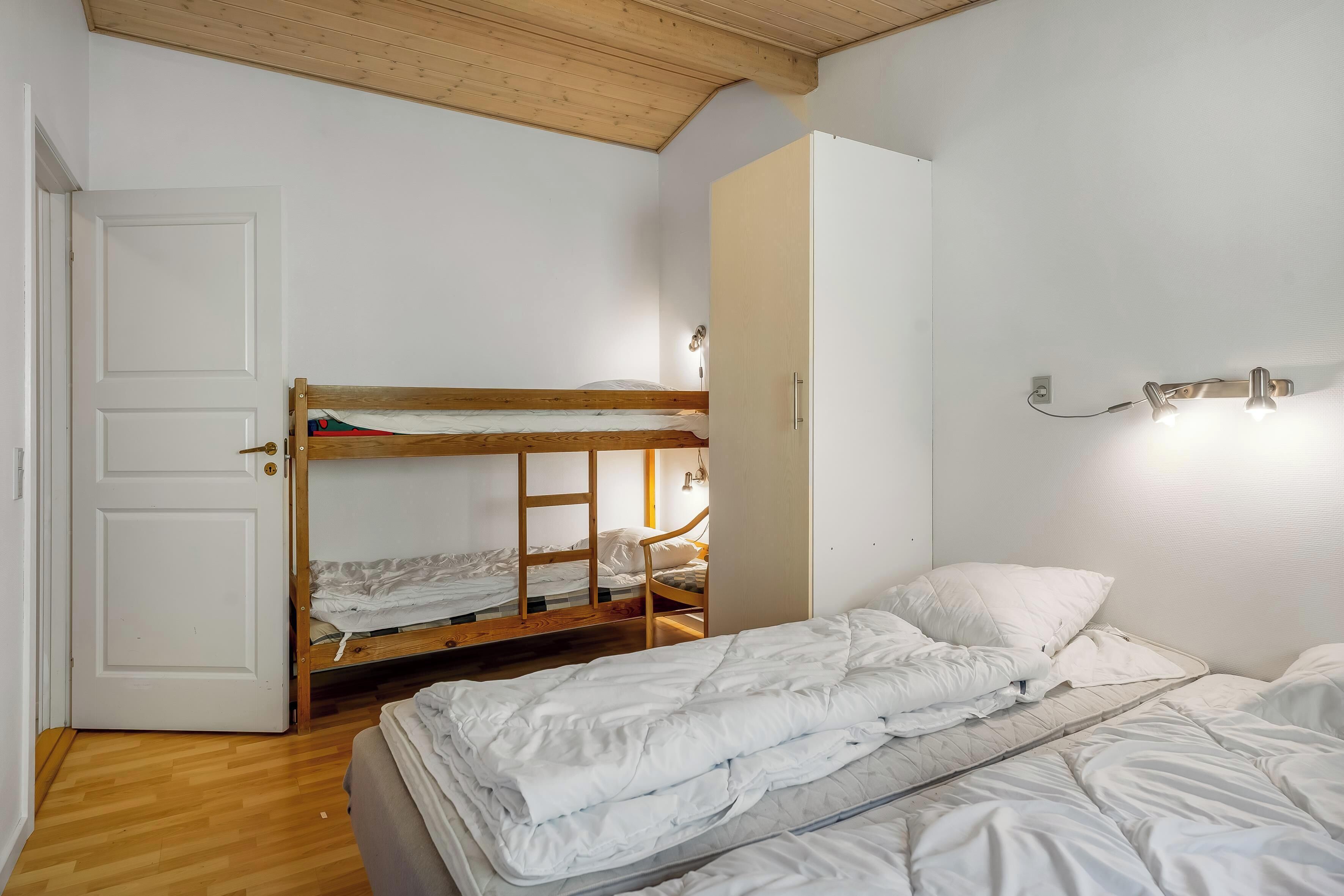 Een slaapkamer met een stapelbed, een eenpersoonsbed, een houten deur en een lamp.