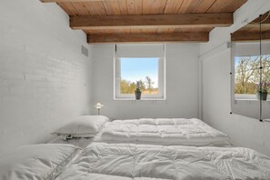 Ein Zimmer mit Holzbalkendecke, weißen Backsteinwänden, einem großen Fenster mit Aussicht und einem Bett mit weißer Bettwäsche.