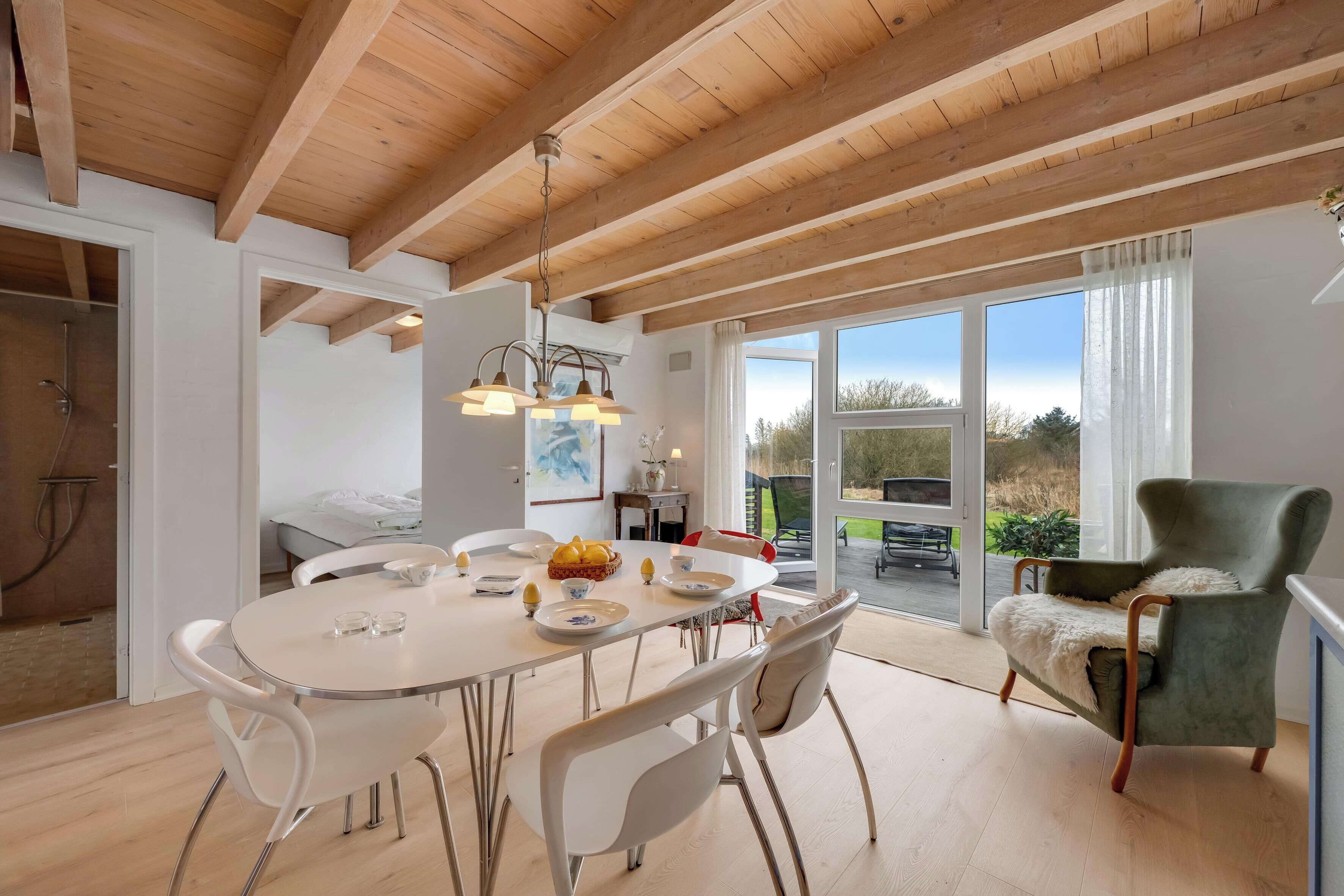 Een modern interieur met een eethoek, een groene fauteuil en uitzicht door een glazen deur.