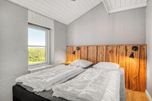 Ein Schlafzimmer mit großem Fenster, Holz-Kopfteil und einem Bett mit weißer Bettwäsche.