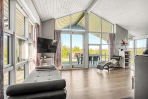 Ein geräumiges Zimmer mit großem Fenster, einer Couch, einem Relaxsessel und einem Fernseher.