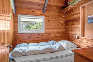 A wooden cabin room with a bed, a window, and a wooden ceiling. - Cozy holiday home with wood-burning stove in Klitmøller (Thisted)