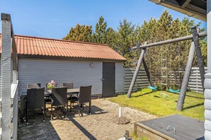 A patio with a table and chairs, a swing set, and a shed. - Cozy holiday home with wood-burning stove in Klitmøller (Thisted)