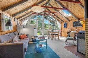 A cozy loft-style room with a high ceiling, wooden beams, a sofa, a dining table, and a TV. - Cozy holiday home with wood-burning stove in Klitmøller (Thisted)