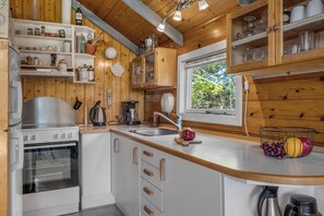 A kitchen with wooden cabinets, a stainless steel stove, a sink, and a window with a view of greenery. - Cozy holiday home with wood-burning stove in Klitmøller (Thisted)
