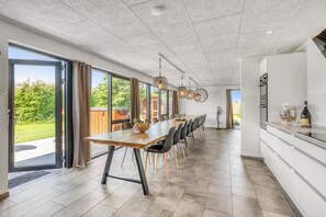 Een moderne keuken met een lange eettafel, grote ramen en uitzicht op de omgeving.