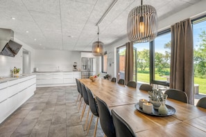 Une cuisine moderne avec des meubles blancs, un grand îlot central et un coin repas comprenant une table et des chaises en bois.