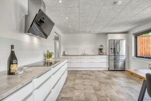 Una cocina moderna con muebles blancos, un refrigerador de acero inoxidable y una ventana con vista a la vegetación.