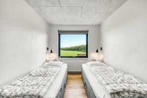 Ein kleines, modernes Schlafzimmer mit zwei Einzelbetten, einem großen Fenster mit Blick auf Grünflächen und einem Heizkörper unter dem Fenster.