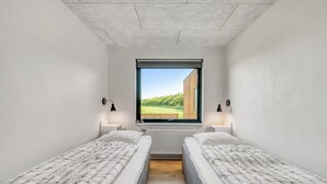 Ein Zimmer mit zwei Einzelbetten, einem Fenster mit Blick auf Grünflächen und einem Heizkörper unter dem Fenster.