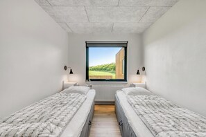 Een kamer met twee eenpersoonsbedden, een raam met uitzicht op groen en een radiator onder het raam.