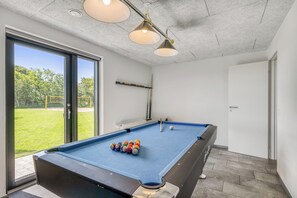 Ein Billardtisch mit Kugeln, ein Billardständer und eine Tür, die nach draußen führt.