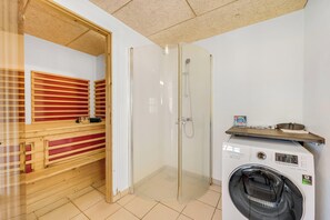 Ein Zimmer mit einer hölzernen Sitzbank, einer Duschkabine aus Glas und einem Frontlader-Waschmaschine.