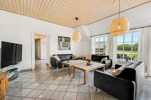 Ein großzügiger Wohnbereich mit Fernseher, Sofa und Tisch, großen Fenstern mit Aussicht und einer Holzbalkendecke.