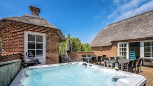 Jacuzzi en un patio trasero con una casa de ladrillo y construcciones de techo de paja.