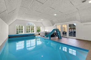 An indoor swimming pool with a slide, large windows, and a staircase leading to an outdoor area. - Large holiday home with pool, hot tub and activity room in Husby (Ulfborg)