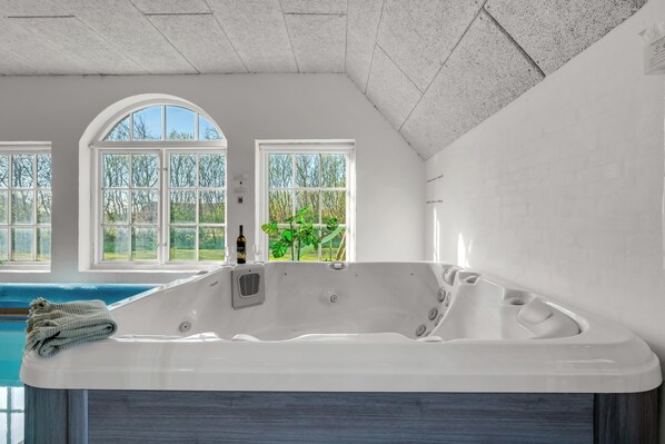 Ein Wellnessraum mit einer großen Badewanne, einem Fenster und Blick ins Freie.