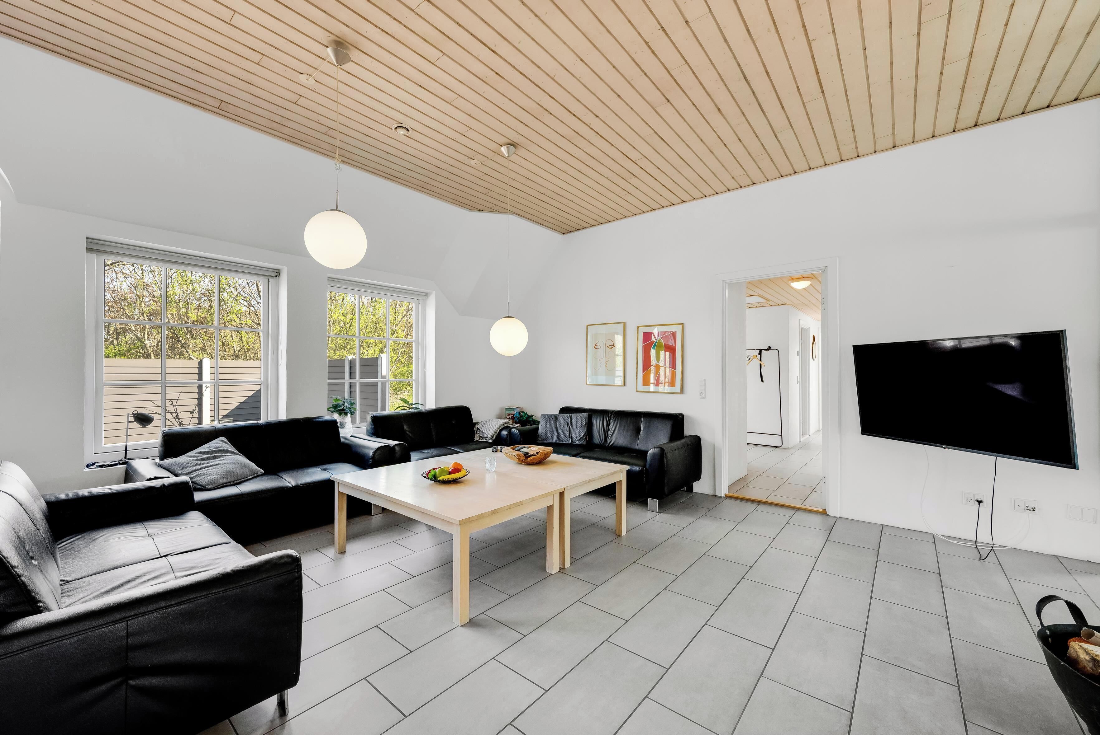 A modern living room with a wooden ceiling, black leather sofas, a coffee table, and a flat-screen TV.