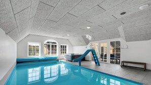 Piscina interna com escorregador, grandes janelas e um banco.