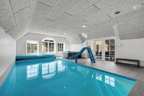 An indoor swimming pool with a slide, large windows, and a bench. - 18-person pool house with hot tub, infrared sauna and activity room. (Ulfborg)
