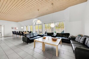 Ein geräumiger Wohnbereich mit Holzboden, schwarzen Ledersofas, einem Holztisch und großen Fenstern.