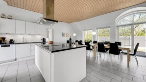 Uma cozinha moderna com armários brancos, uma ilha central e uma área de refeições com mesa e cadeiras.