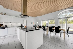 A modern kitchen with white cabinets, a central island, and a dining area with a table and chairs. - 18-person pool house with hot tub, infrared sauna and activity room. (Ulfborg)