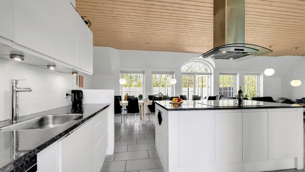 Uma cozinha moderna com armários brancos, uma ilha central e uma área de refeições com luz natural.