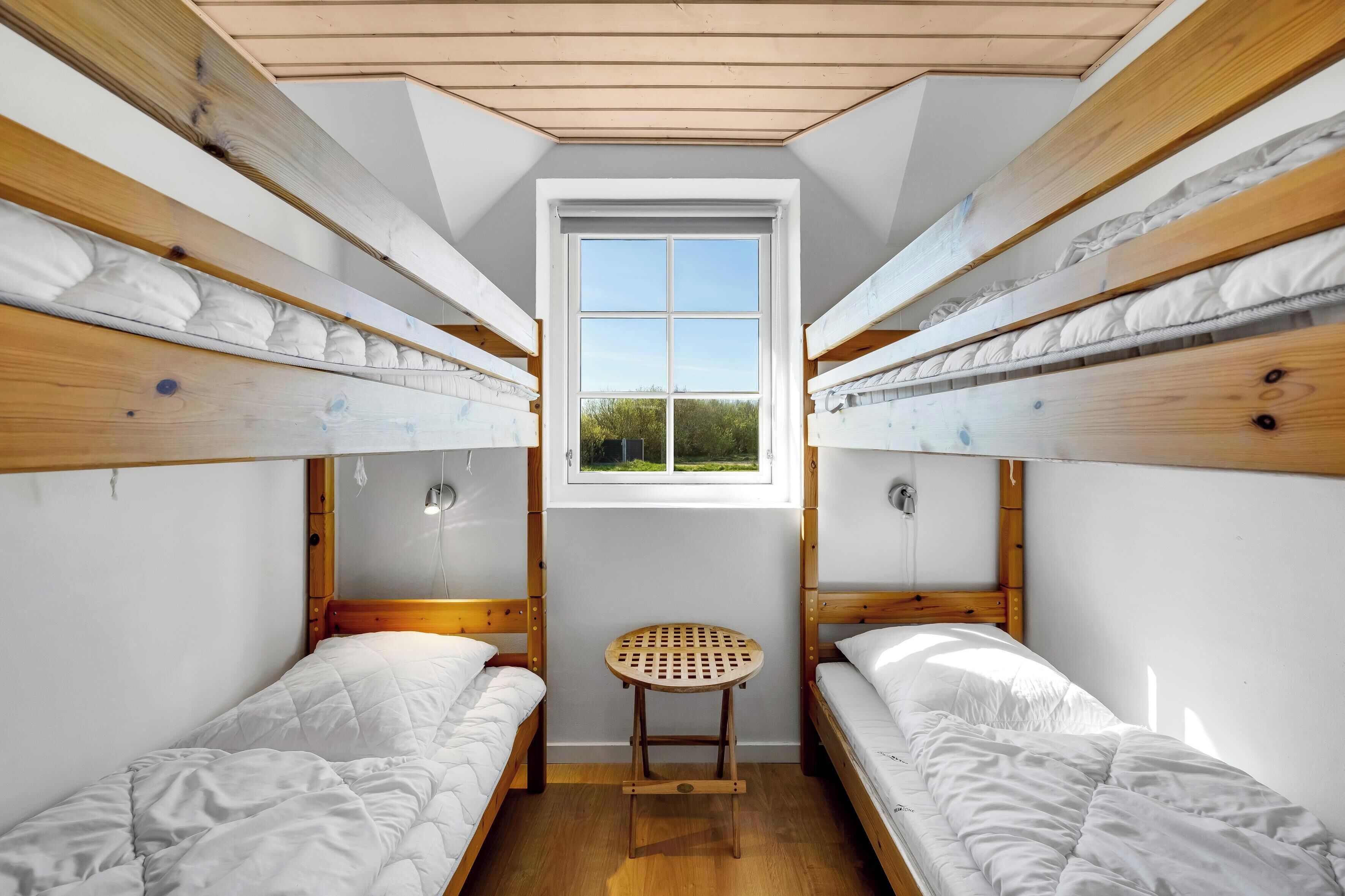 Ein Schlafsaalzimmer mit Etagenbetten, einem kleinen Holzschemel und einem Fenster.