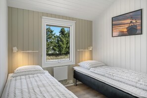 Ein Schlafzimmer mit zwei Betten, einem Fenster mit Blick auf Bäume und einem Bild eines Bootes an der Wand.