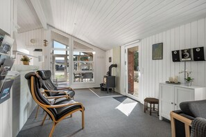 A modern interior with a fireplace, seating area, and a view through large windows. - Holiday home with sauna and enclosed terrace in Vorupør. (Thisted)