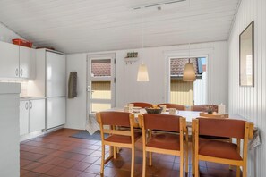 Ein Essbereich mit einem Tisch für vier Personen, Holzstühle, einer hängenden Pendelleuchte und einem Kühlschrank im Hintergrund.