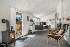 A modern interior with a wood-burning stove, a leather chair, and a television in a cozy living area. - Holiday home with sauna and enclosed terrace in Vorupør. (Thisted)