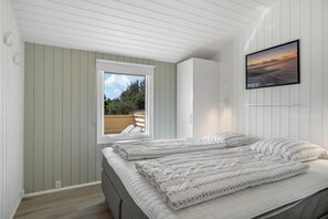 A bedroom with a bed, a window, a wall-mounted TV, and a view of the outdoors. - Holiday home with sauna and enclosed terrace in Vorupør. (Thisted)
