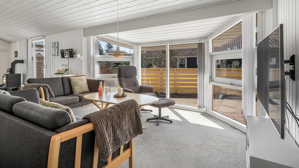 Een moderne woonkamer met een bank, salontafel, stoelen, grote ramen en een schuifpui die leidt naar een buitenruimte.