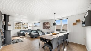 En moderne stue med sofa, spisebord, stole, pejs og store vinduer.