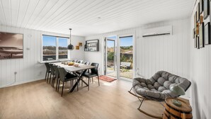 Et spiseområde med et bord og stole, en grå polstret stol og udsigt gennem glasdørene.