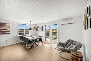 A dining area with a table and chairs, a grey upholstered chair, and a view through the glass doors. - Holiday home with enclosure for dogs, 500 meters from the North Sea (Ringkøbing)