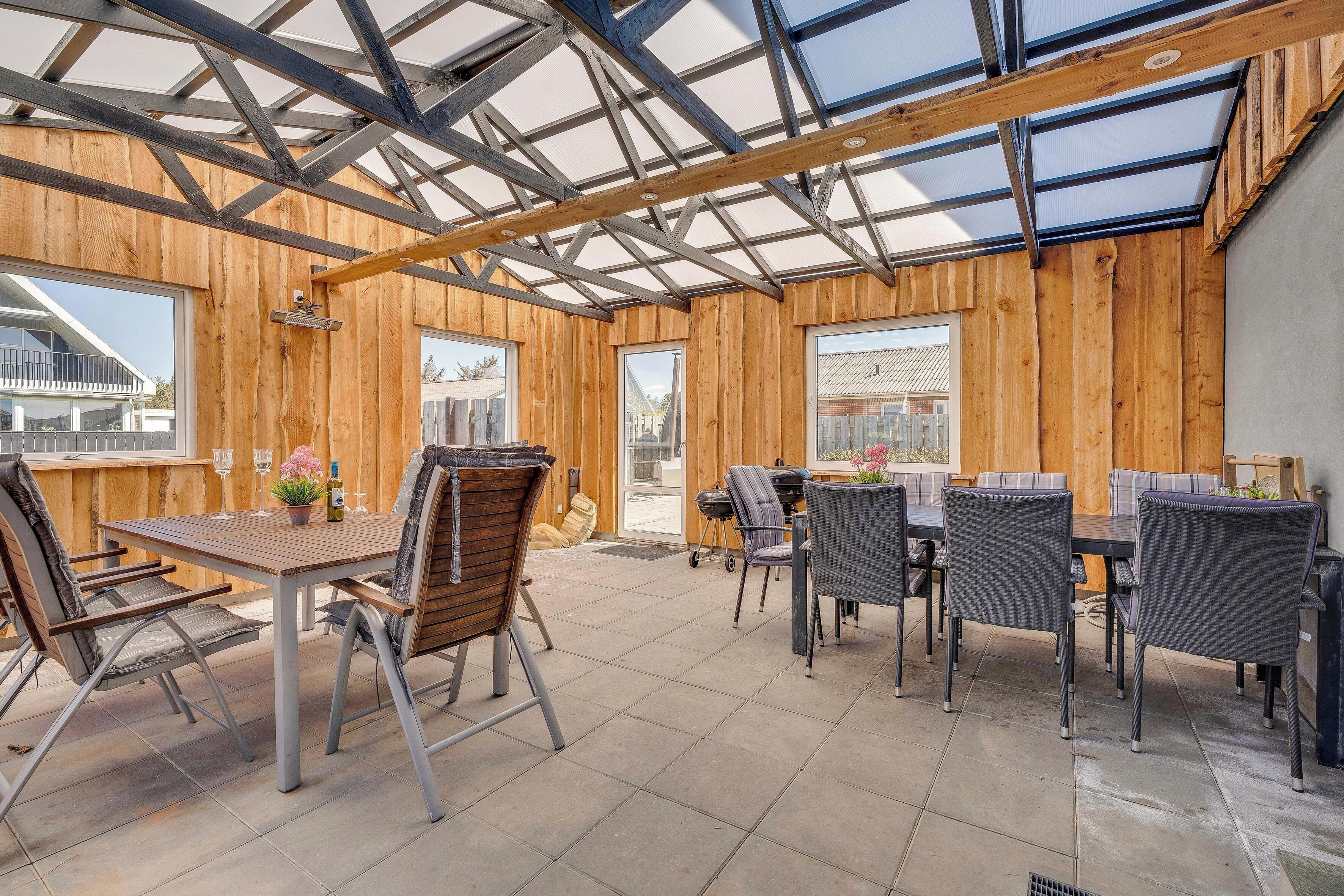 A covered patio with wooden walls, a table with chairs, and a grill.