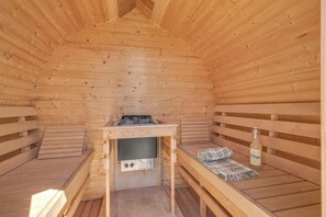 A sauna room with wooden benches, a bench heater, and a bottle of alcohol. - 14-person holiday home in Agger with wilderness bath and outdoor sauna (Vestervig)