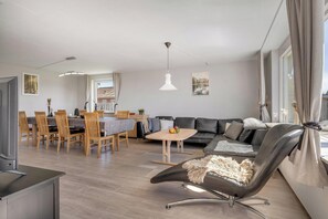 Ein modernes Wohnzimmer mit einer Couch, einem Esstisch, Stühlen und einem Fernseher.