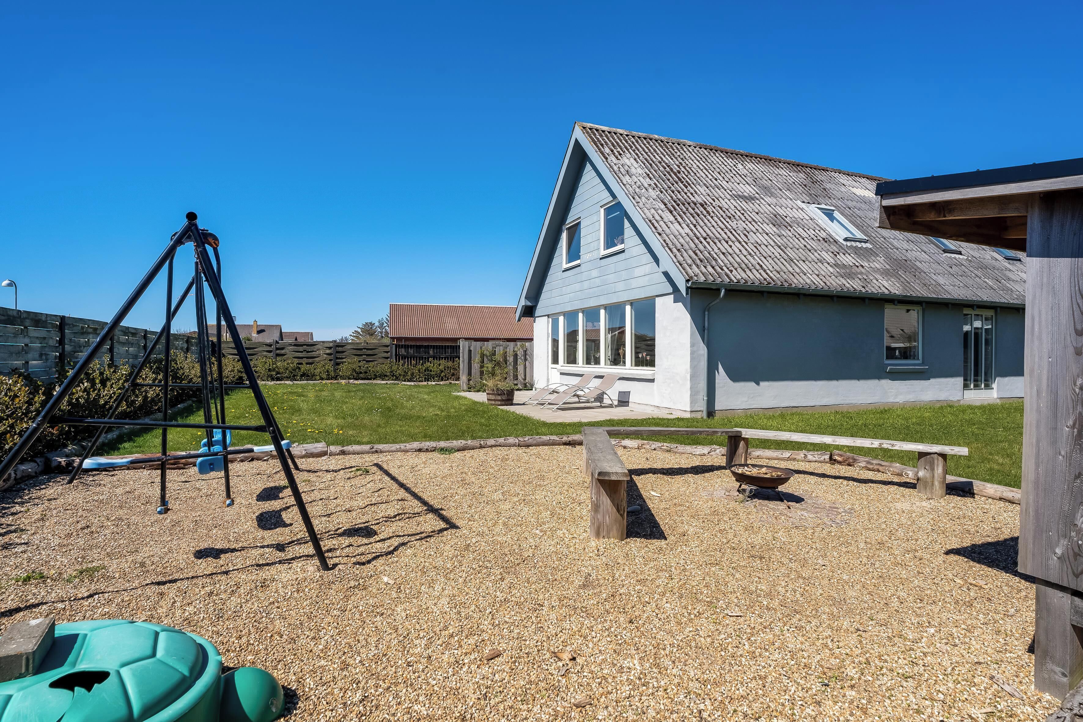 Een speeltuin met schommels en een glijbaan, een picknicktafel en een gebouw met een schuin dak.