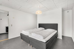 Ein modernes Schlafzimmer mit einem grauen Bett, weißer Bettwäsche und einer Deckenleuchte.