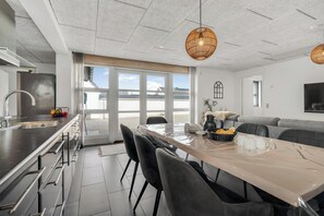 A modern kitchen with a large island, a dining area with a table and chairs, and a grey sofa. - Renovated holiday home with enclosed terrace, centrally located in Vorupør (Thisted)