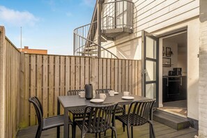 A patio with a table set for four, surrounded by chairs, and a wooden fence. - Renovated holiday home with enclosed terrace, centrally located in Vorupør (Thisted)