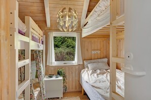 A wooden room with bunk beds, a window with a view of greenery, a bedside table with a plant, and a decorative light fixture. - Family-friendly cottage with shared activities such as swimming pool, tennis. (Fjerritslev)