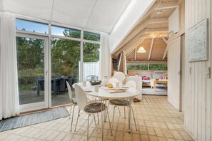 A modern interior with a round dining table, white chairs, and a large sliding glass door leading to an outdoor area. - Family-friendly cottage with shared activities such as swimming pool, tennis. (Fjerritslev)